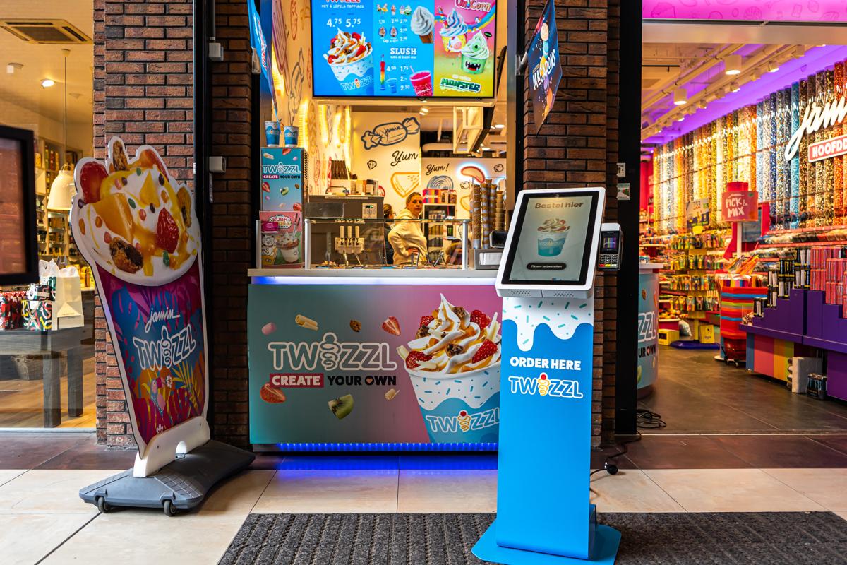 Onesix Kiosk im eigenen Design am Eingang eines Eis- und Süßwarenladens, mit einer Mitarbeiterin hinter dem Tresen
