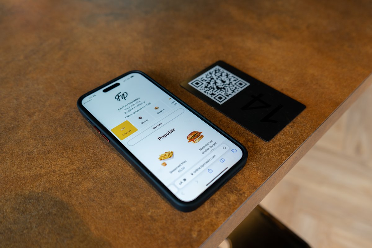 Smartphone mit der digitalen Speisekarte des Online-Kiosk neben einem QR-Tischkärtchen in einem Gastrobetrieb
